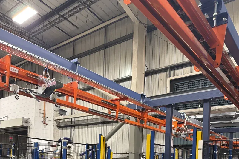 Close-up of curved orange MCM Autotrack overhead conveyor track within an automotive manufacturing facility